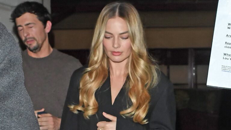 Margot Robbie accessorizes her classy black overcoat with Barbie pink shoes and a clutch while dining with her husband and friends in London.